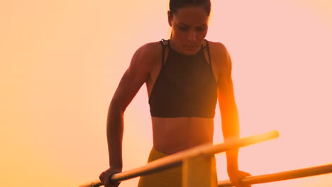 Slow-motion:-a-Beautiful-woman-athlete-doing-push-UPS-on-bars-in-a-black-tank-top-in-great-shape-and-yellow-pants-with-dark-hair.